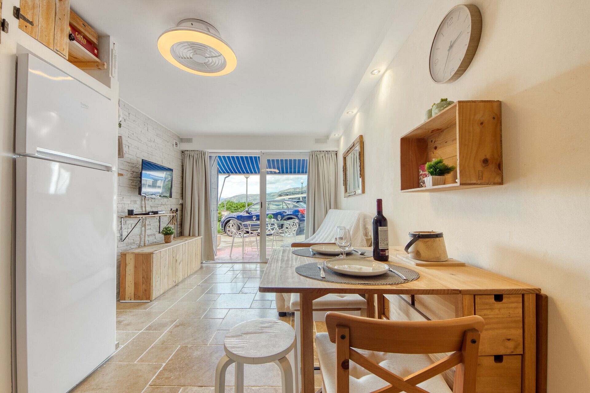 A modern kitchen with a dining area, a wooden cabinet, a clock, and a view of the outside.