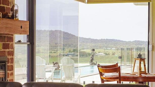 A modern living room with a leather sofa, a table with champagne glasses, and a view of a pool and hills. - Big Sky Country Views  (Boyland)