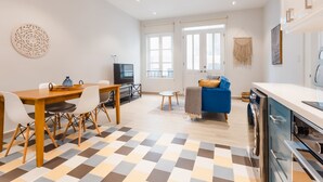 Un salon moderne avec une table à manger en bois, des chaises blanches, un canapé bleu et un coin cuisine équipé d’un lave-linge.