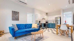 Un appartement moderne avec un canapé bleu, une table à manger avec des chaises, un coin cuisine et un sol à carreaux.