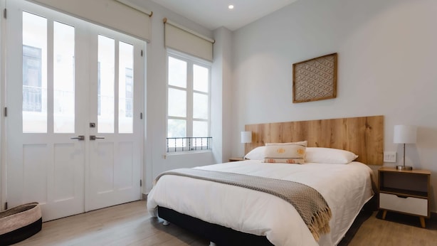 Une chambre à coucher avec un grand lit, une tête de lit en bois, des tables de chevet et une fenêtre avec des stores.