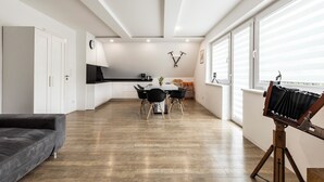 Ein modernes Wohnzimmer mit einem dunklen Sofa, einem Essbereich mit Tisch und Stühlen sowie einem großen Fenster mit Jalousien.