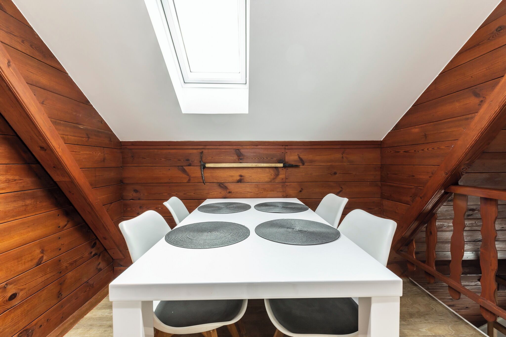 Una mesa blanca con cuatro individuales negros y seis sillas blancas en una habitación de madera con techo inclinado y tragaluz.