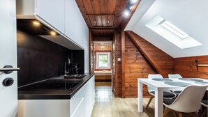 Eine kompakte Küche mit modernen Geräten, ein Essbereich mit weißem Tisch und Stühlen sowie eine schräge Decke mit Dachfenstern.