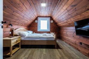 A cozy attic bedroom with a wooden sloped ceiling, a single bed, a nightstand, a TV mounted on the wall, and a window providing natural light. - Apartamenty Taternickie (Zakopane)