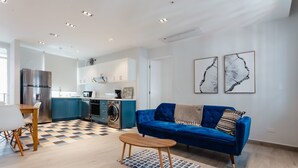 Un salon moderne avec un canapé bleu, une table basse en bois et un coin repas comprenant une table et des chaises blanches.