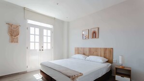 A bedroom with a wooden headboard, a bed with white linens, a bedside table with a lamp, and a macramé wall hanging. - w* | Perfect 2BR in Casco Antiguo w/ Balcony (Panamá)
