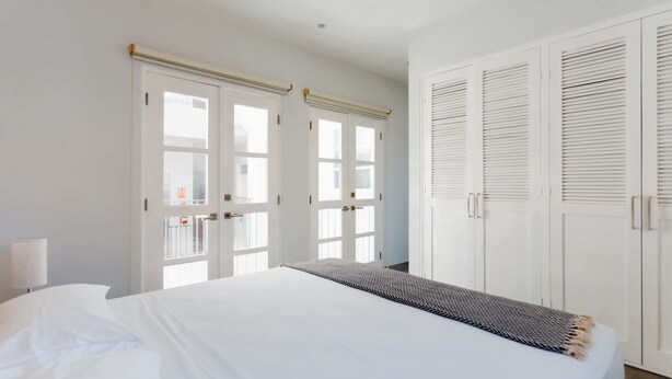 A bedroom with a large bed, white walls, and a wardrobe with louvered doors. - w* | Perfect 2BR in Casco Antiguo w/ Balcony (Panamá)