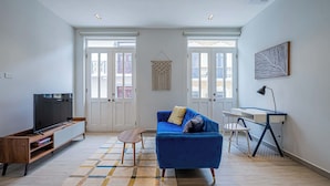 A modern living room with a blue sofa, a TV, and a desk with a lamp. - w* | Airy 1BR w/ Balcony in Panama (Panamá)