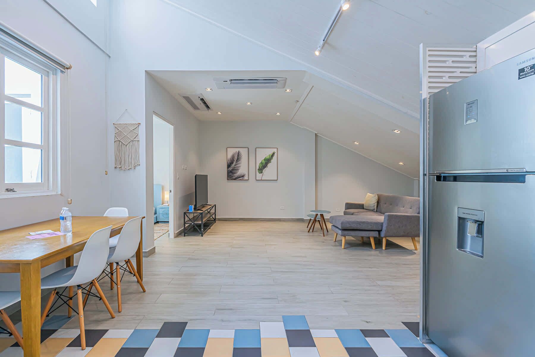 A modern kitchen with a built-in refrigerator, a dining area with a wooden table and chairs, and a living area with a sofa and a TV.