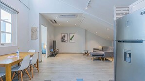 Eine moderne Küche mit Einbaukühlschrank, ein Essbereich mit Holztisch und -stühlen sowie eine Wohnbereich mit Sofa und Fernseher.