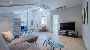 Ein geräumiger Wohnbereich mit einer Couch, zwei kleinen Tischen, einem Fernseher und einer Küche im Hintergrund.