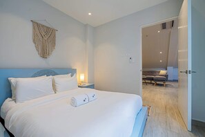 Un dormitorio moderno con una cama grande, una mesita de noche con lámpara y un colgador de macramé en la pared.