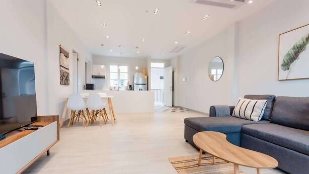 A modern living room with a grey sofa, a wooden coffee table, and a TV on a wooden stand. There is a dining area with a white table and chairs. - w* | Vivid 1BR w/ Magical lighting in Panama (Panamá)
