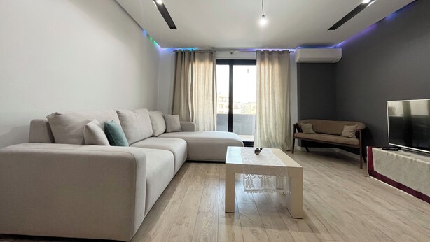 A modern living room with a sectional sofa, a coffee table, a TV, and a balcony view. - 2 Bedroom Apartment Tirana/ Family friendly (Tirana)