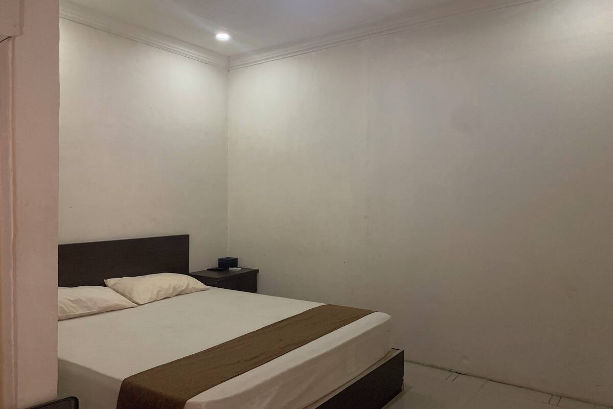 A hotel room with a single bed, a nightstand, and a wall-mounted light.