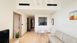 Un salon moderne comprenant un canapé, une table à manger avec des chaises, un coin cuisine visible à travers une porte ouverte, et un téléviseur à écran plat posé sur un meuble.