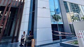 Un immeuble moderne de grande hauteur, doté d’une façade en verre, d’une entrée imposante avec un portail de sécurité et d’une borne d’incendie bien visible au niveau du sol.