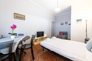 A hotel room with a bed, a TV, a dining table with chairs, a potted plant, and a sofa. - Magi Apartment in Rome (Rome)