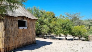 Una cabaña de techo de paja con un letrero que dice 'RECEPTION' y una ventana.