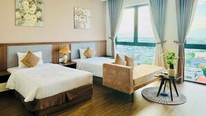 A hotel room with two beds, a sofa, a small table, and a view of the city. - ATP Galaxy Hotel & Apartment Danang (Da Nang)