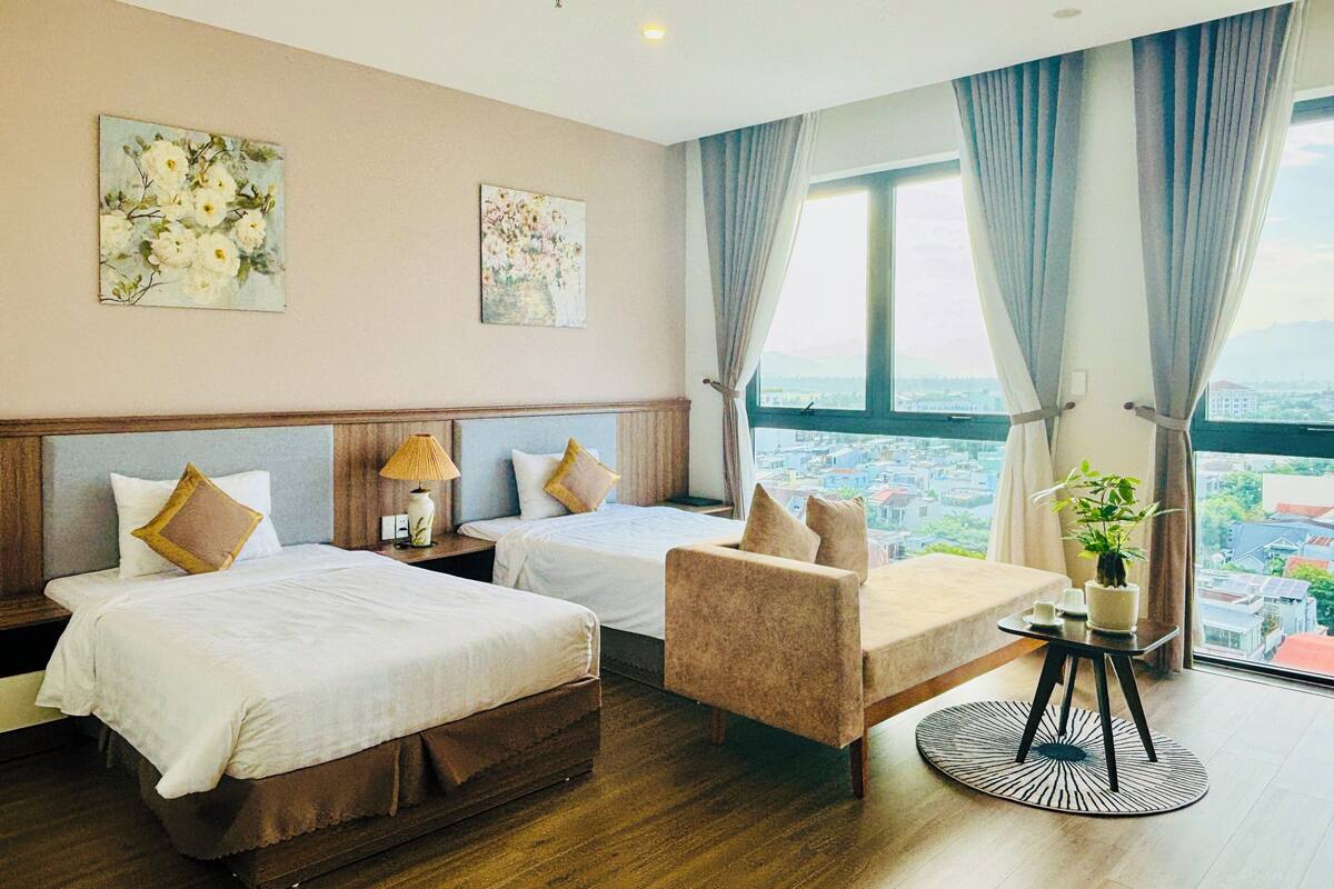 A hotel room with two beds, a sofa, a small table, and a view of the city.