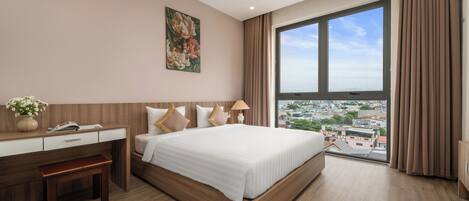 A modern hotel room with a large bed, a desk, and a view of a cityscape through a large window.