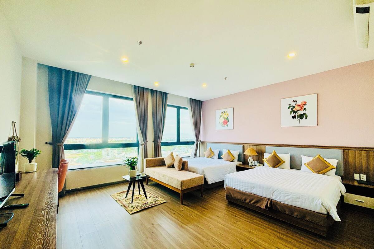 A hotel room with two beds, a sofa, a desk, and a view of the city.