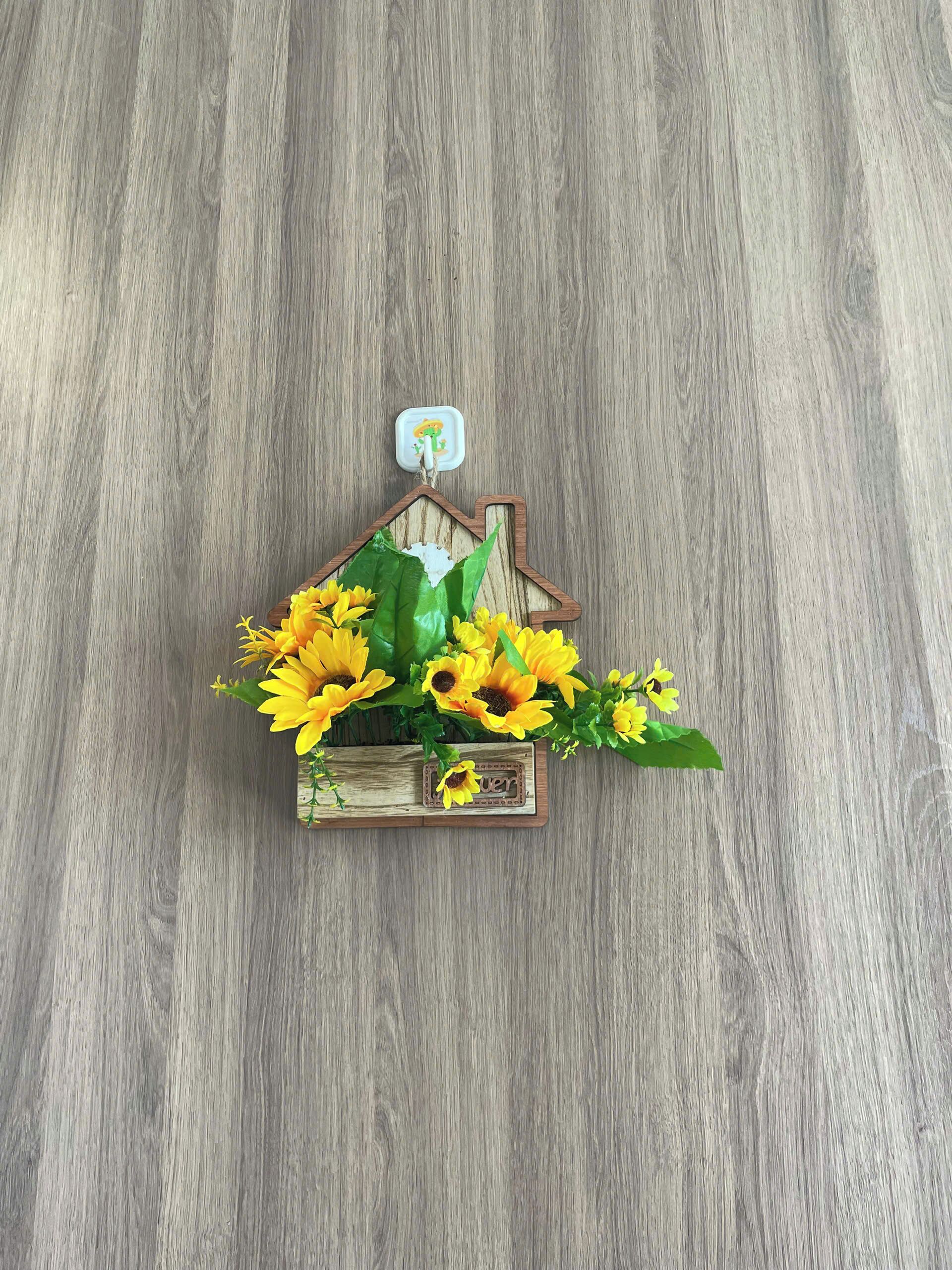 En trälåda formad som ett hus, med gula blommor, placerad på ett trägolv.