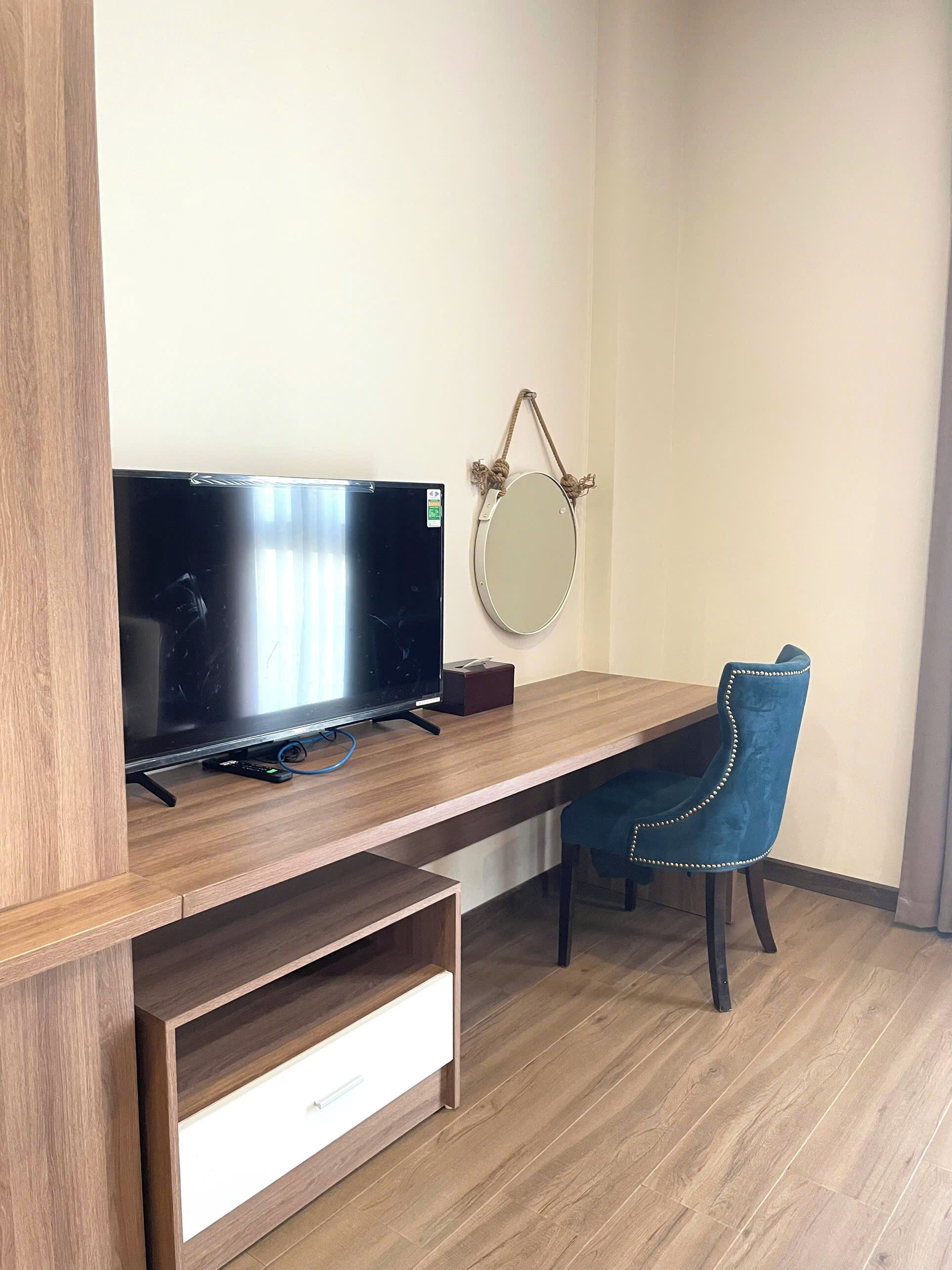 A modern room with a wooden desk, a television, a mirror, and a blue chair.