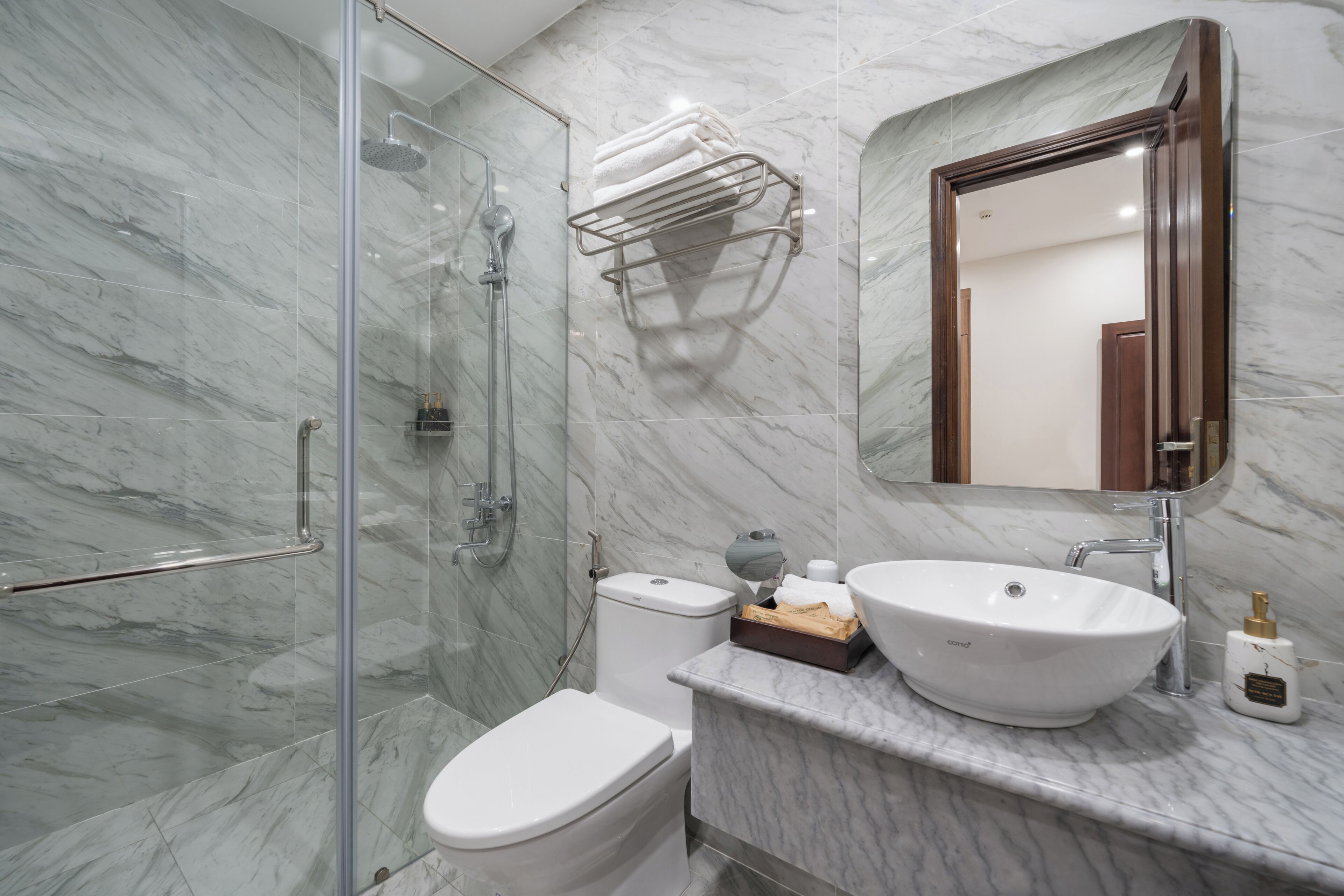 A modern bathroom with a glass shower enclosure, a toilet, a sink with a marble countertop, and a towel rack.