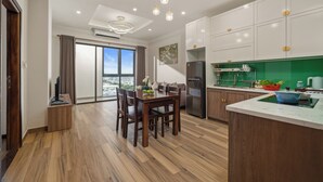 A modern kitchen with wooden cabinets, a central island, and a large window offering a city view. - ATP Galaxy Hotel & Apartment Danang (Da Nang)