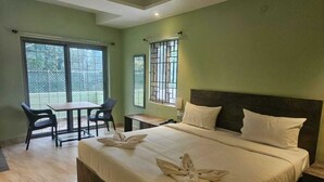 A hotel room with a bed, two chairs, a small table, and a balcony with a view. - Hotel Peppers (Yercaud)
