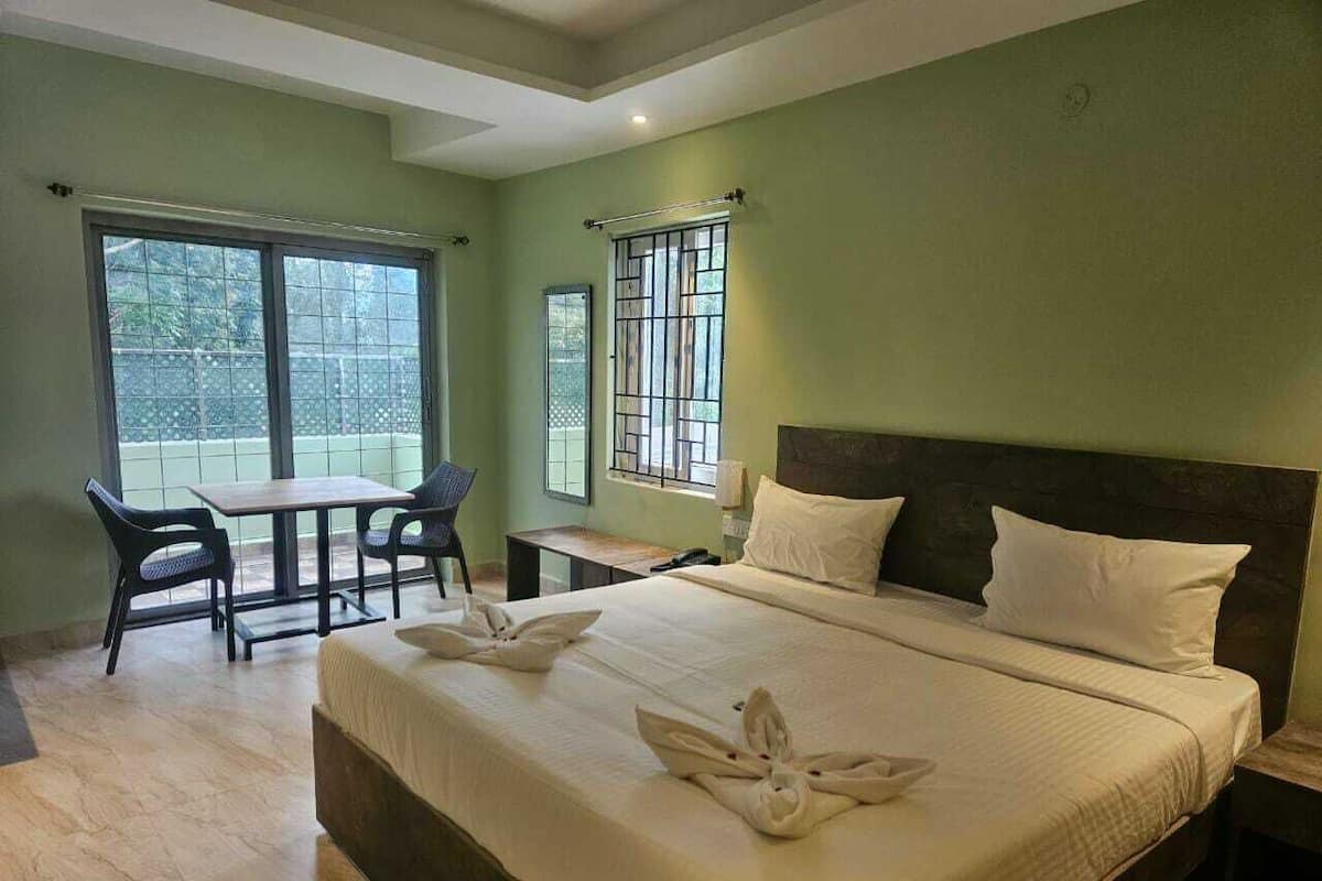 Habitación de hotel con cama, dos sillas, una mesita y balcón con vistas.