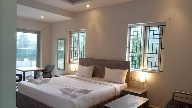 A modern hotel room with a large bed, bedside tables, a desk, and a chair. - Hotel Peppers (Yercaud)