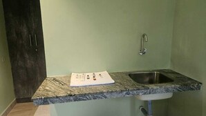 A kitchen with a granite countertop, a stainless steel sink, and a dark wooden door. - Hotel Peppers (Yercaud)
