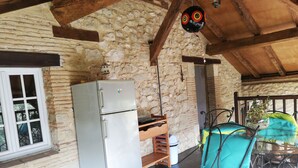 A rustic stone building with a wooden ceiling, a white-framed window, and a silver refrigerator.