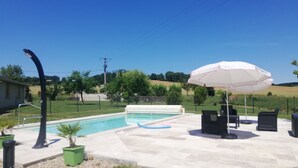 A swimming pool area with a hot tub, outdoor seating, and a white umbrella.