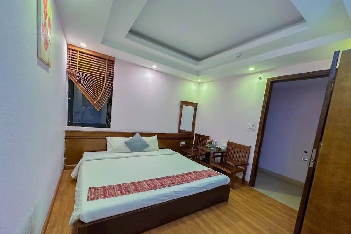 A hotel room with a large bed, wooden flooring, a desk with a chair, a mirror, and a door.