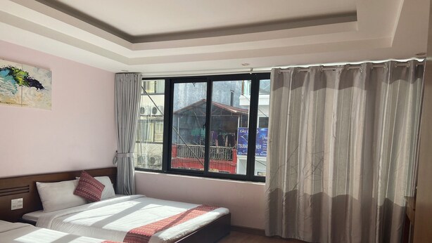 Habitación de hotel con dos camas, un ventanal con cortinas, suelo de madera y un cuadro en la pared.