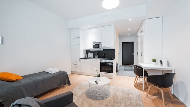 Un espacio habitable moderno y compacto con kitchenette, cama, escritorio y silla.