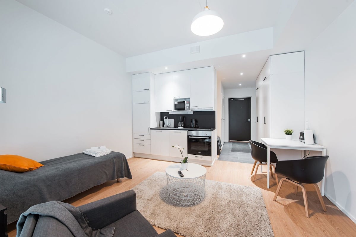 Een moderne, compacte woonruimte met een kitchenette, een bed, een bureau en een stoel.