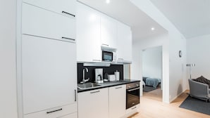 Una cocina moderna con armarios blancos, microondas y cafetera. Cuenta con un pequeño comedor con mesa y sillas.