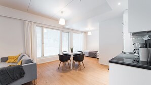 Una sala de estar moderna con un sofá, una mesa de comedor con sillas y una zona de cocina con mostrador y electrodomésticos.
