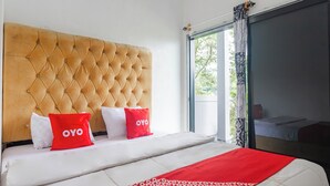 Une chambre d’hôtel avec une tête de lit capitonnée, un lit avec une literie blanche et des touches de rouge, et une vue sur l’extérieur grâce à une grande fenêtre.