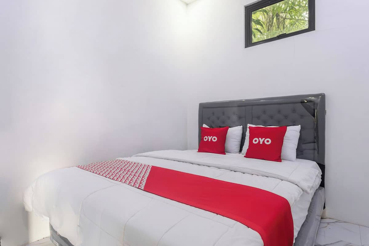 Ein Bett mit grauem Kopfteil, weißer Bettwäsche und zwei roten Kissen mit der Aufschrift 'OYO'.