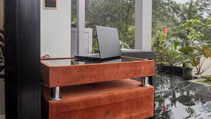 Un ordinateur portable est posé sur un support en bois dans une pièce dont le sol est noir et qui offre une vue sur la verdure à l’extérieur.