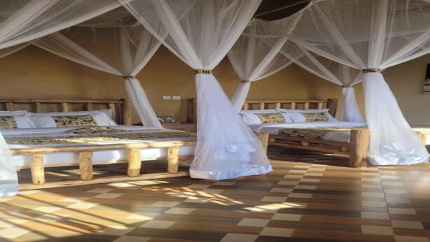 A room with three wooden beds, each with a canopy. The room has a checkered floor and a beige wall. - Stevalyn's Ridge View Lodge (Jinja)
