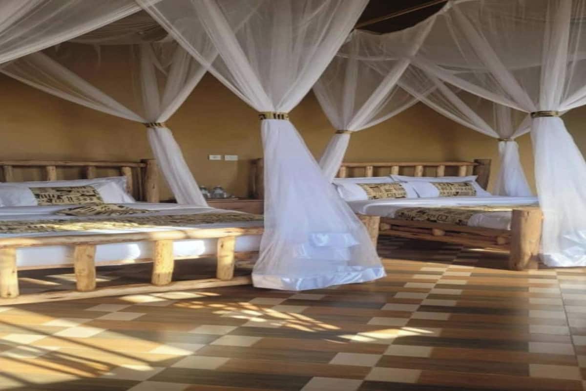 A room with three wooden beds, each with a canopy. The room has a checkered floor and a beige wall.