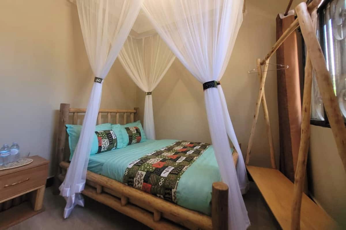A room with a bed under a canopy, a wooden nightstand, and a window with curtains.